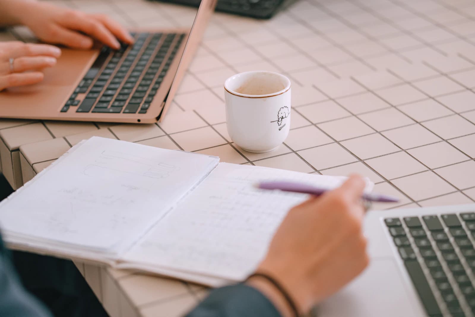 A notebook, laptops and coffee on a shared work table